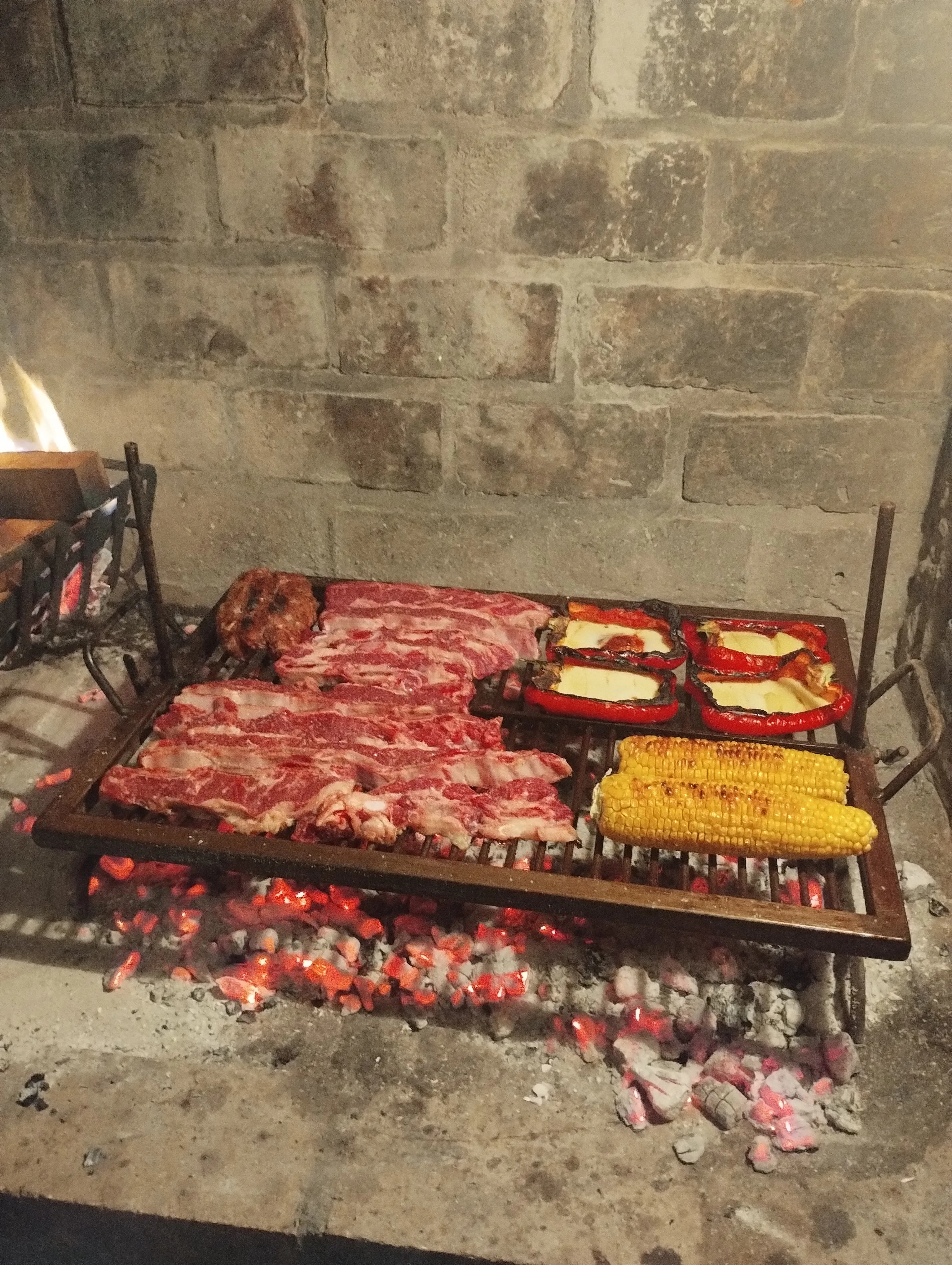 Meat, peppers, and corn grilling over coals on an asado parrilla