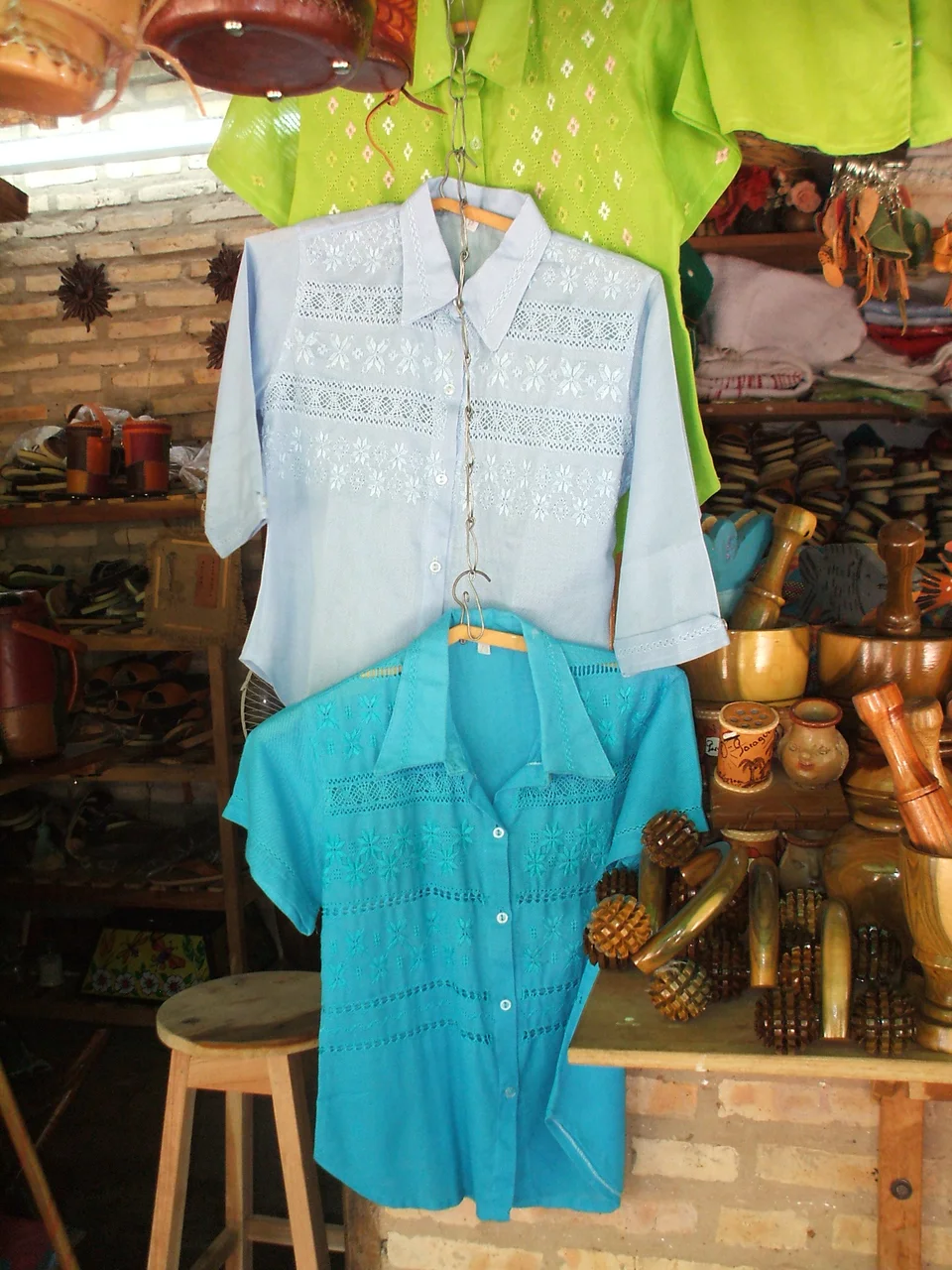 Camisas de ao po’i celestes y turquesas con bordados en una tienda de artesanía