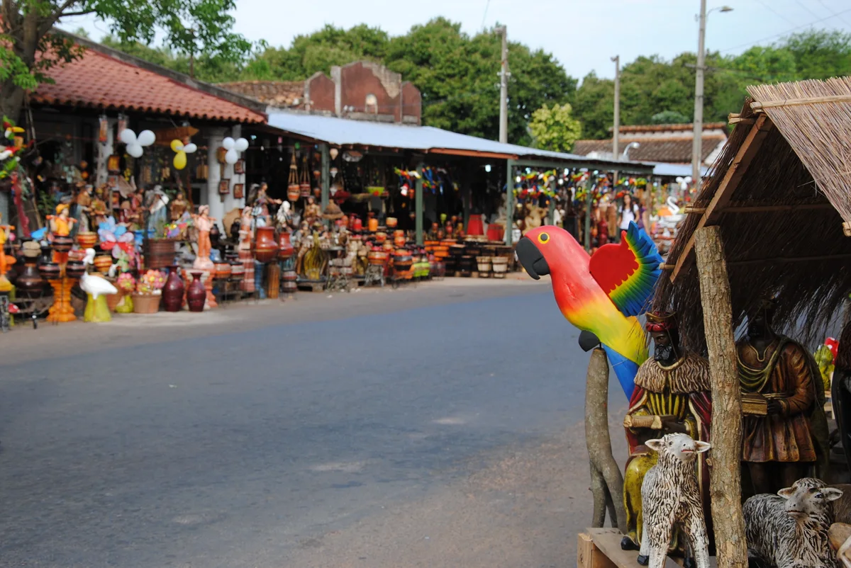 Figuras y macetas de cerámica de colores en puestos junto a una calle de Areguá