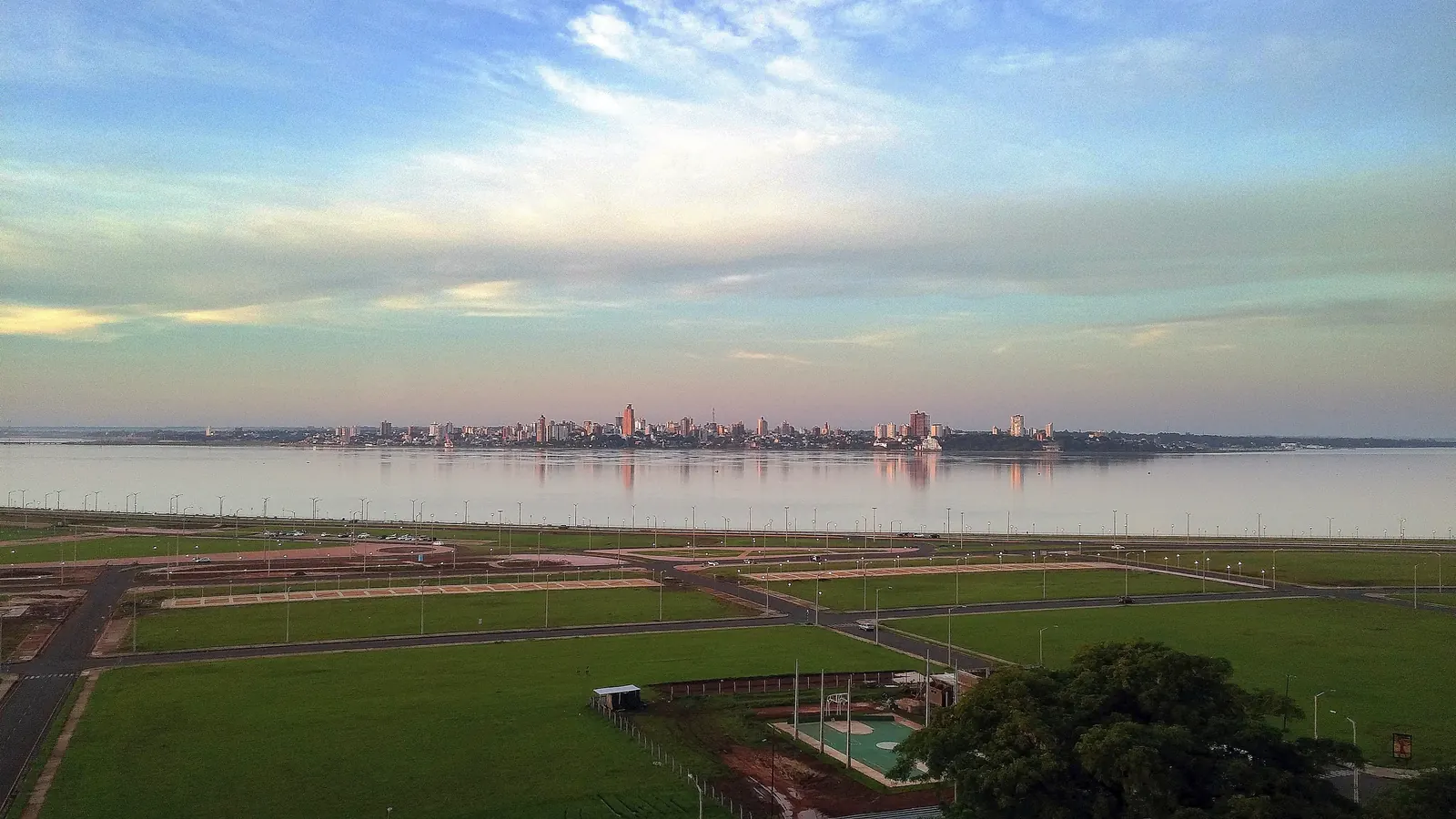 Green lawns of the Costanera in Encarnación, with the Paraná river and the Posadas skyline behind