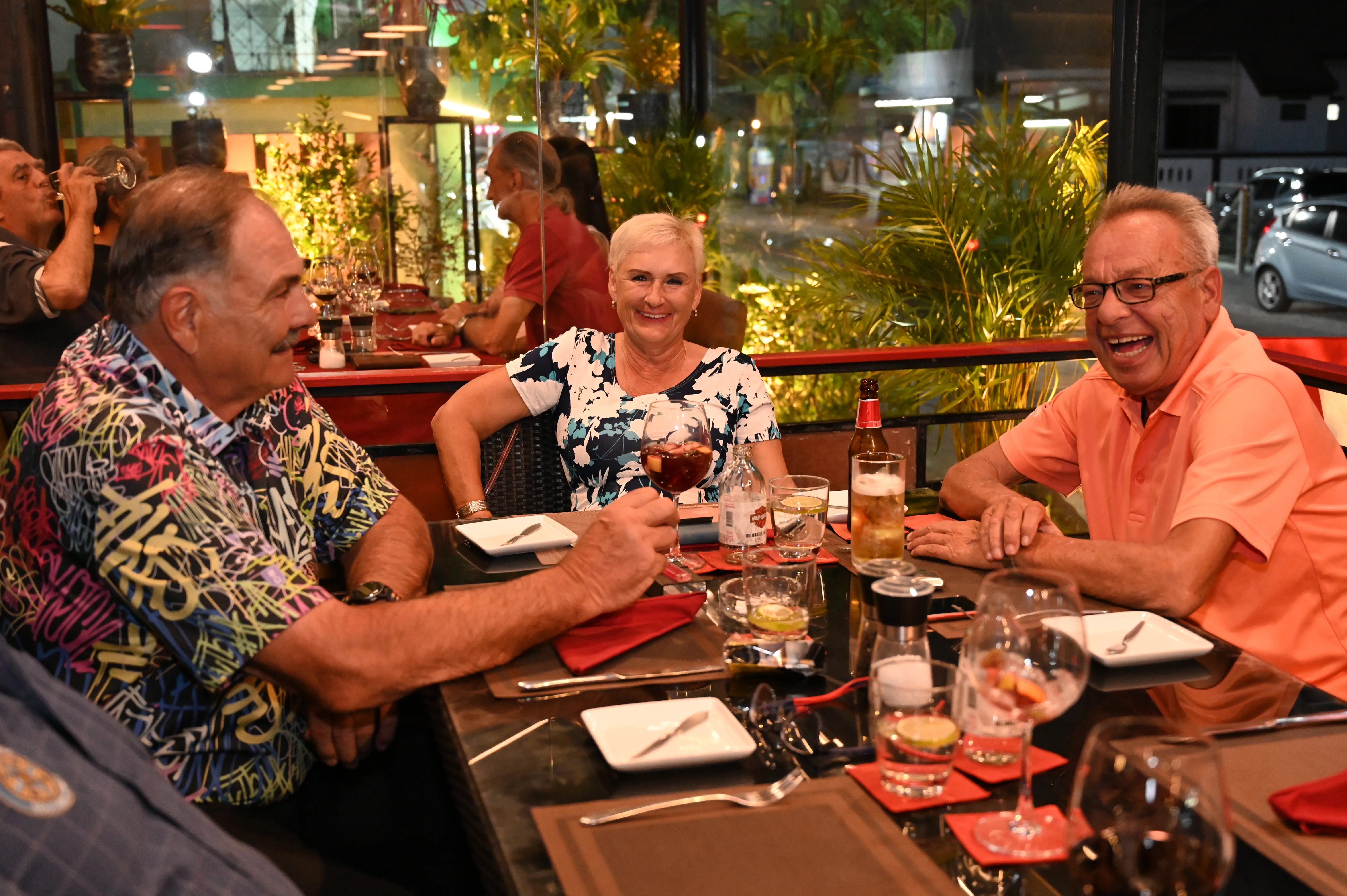 Three friends laughing and toasting over dinner at a restaurant