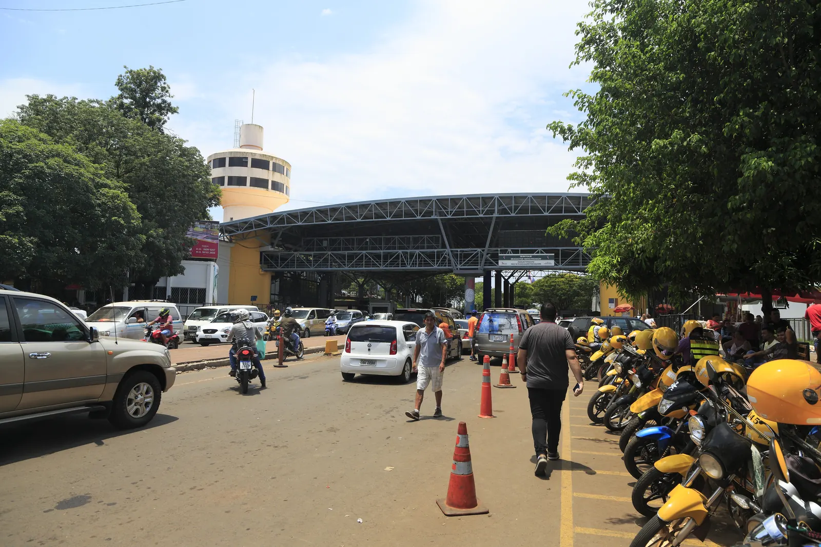 Cars, motorbikes and parked yellow moto-taxis in front of a large checkpoint canopy at the Ciudad del Este end of the Friendship Bridge