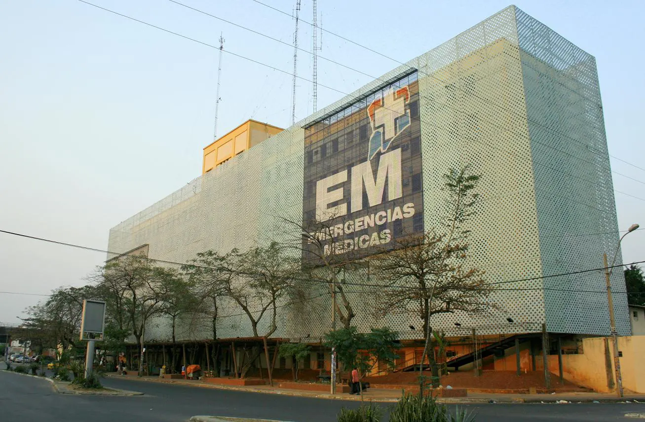 A tall building with a green patterned facade and an Emergencias Médicas sign.