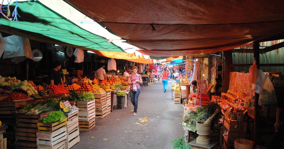 Adentro del Mercado 4, puestos de frutas y verduras bajo toldos de colores.