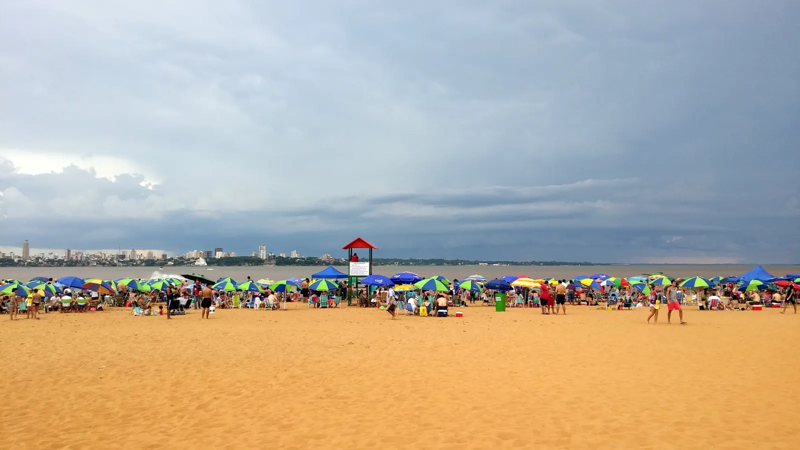 Playa San José in Encarnación, a wide sandy beach with sunshades and a lifeguard tower by the river