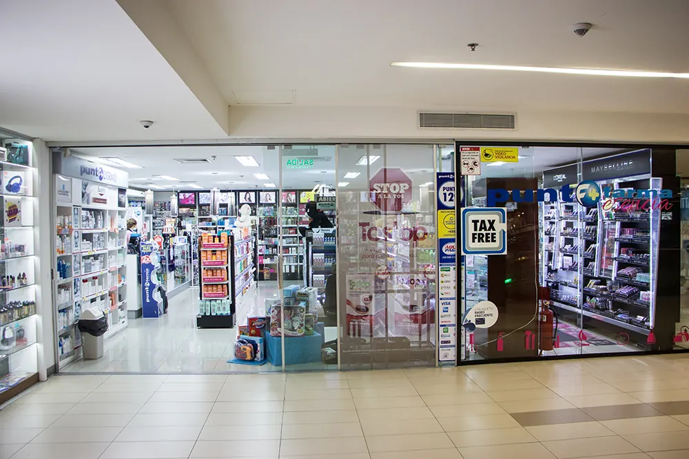 Frente de vidrio de una farmacia Punto Farma dentro de un shopping, con estantes de productos de salud y belleza