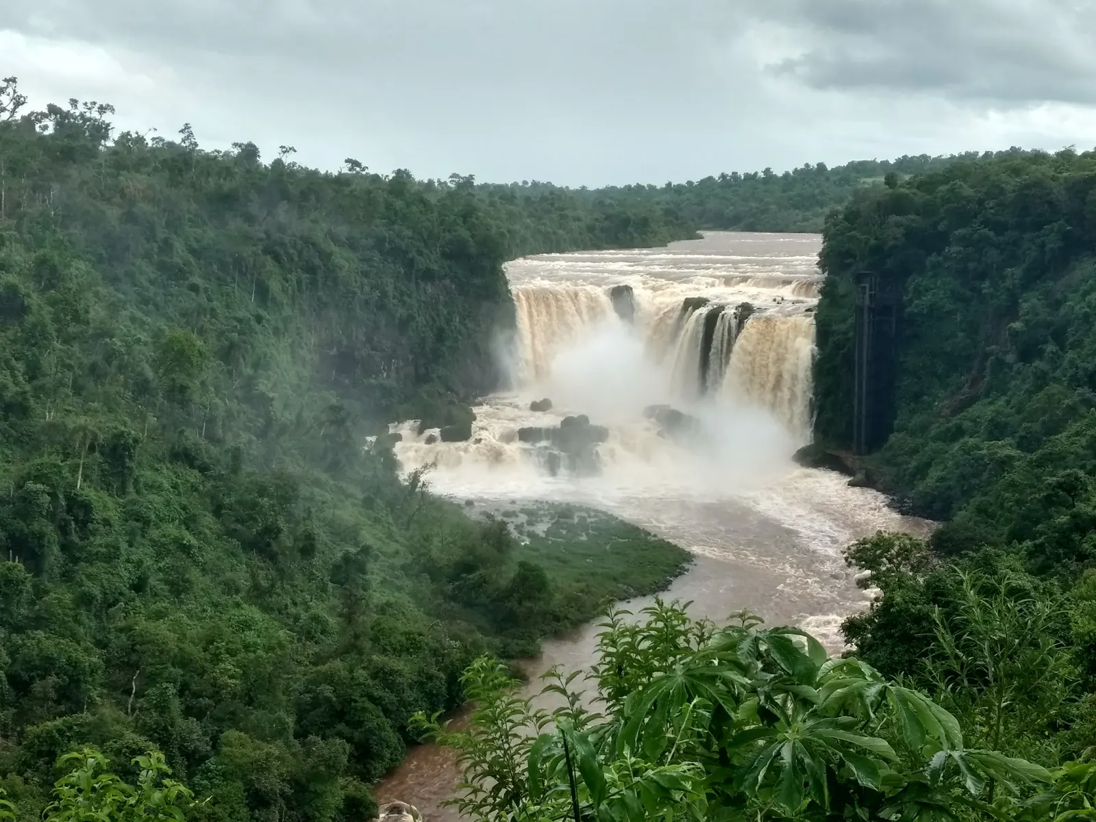 The wide brown Saltos del Monday waterfalls plunging into a green forested gorge, with mist rising