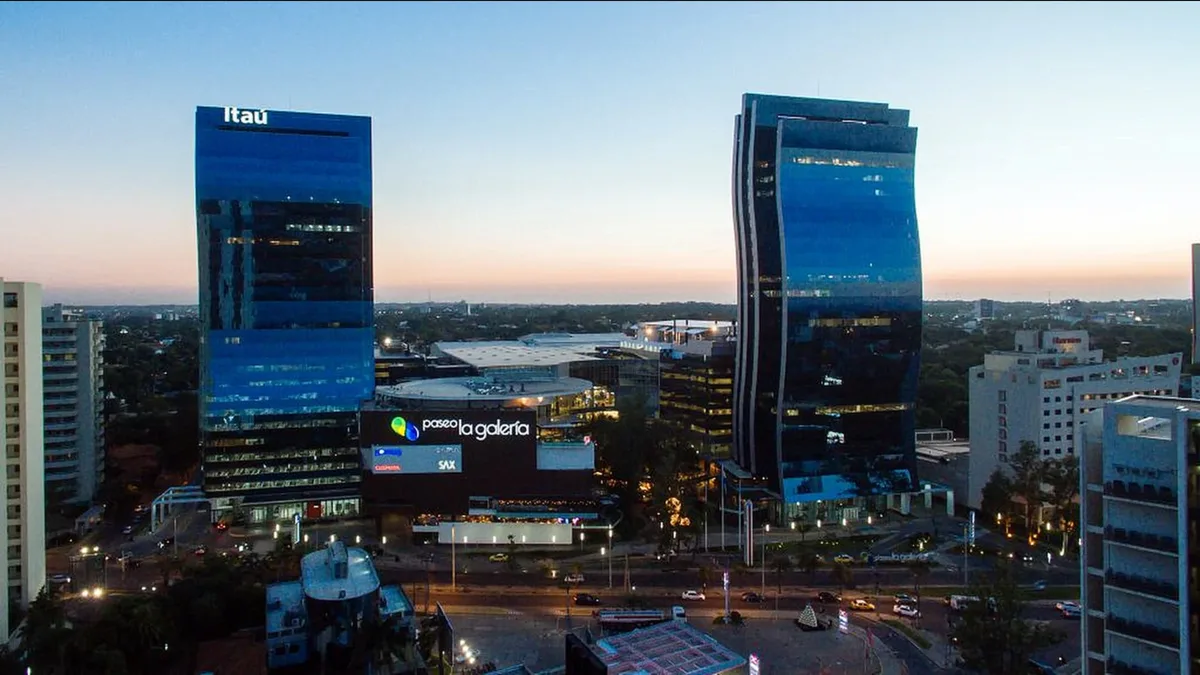 Paseo La Galería shopping complex between two blue-glass towers at dusk