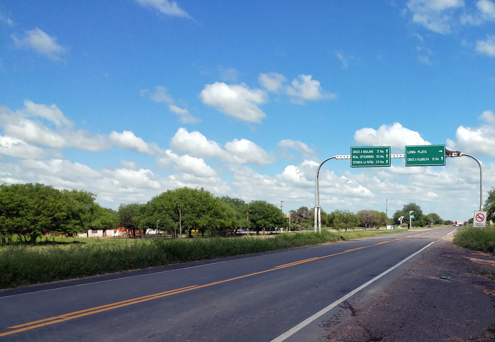 Una ruta asfaltada recta con carteles verdes en el desvío a Loma Plata sobre la Transchaco
