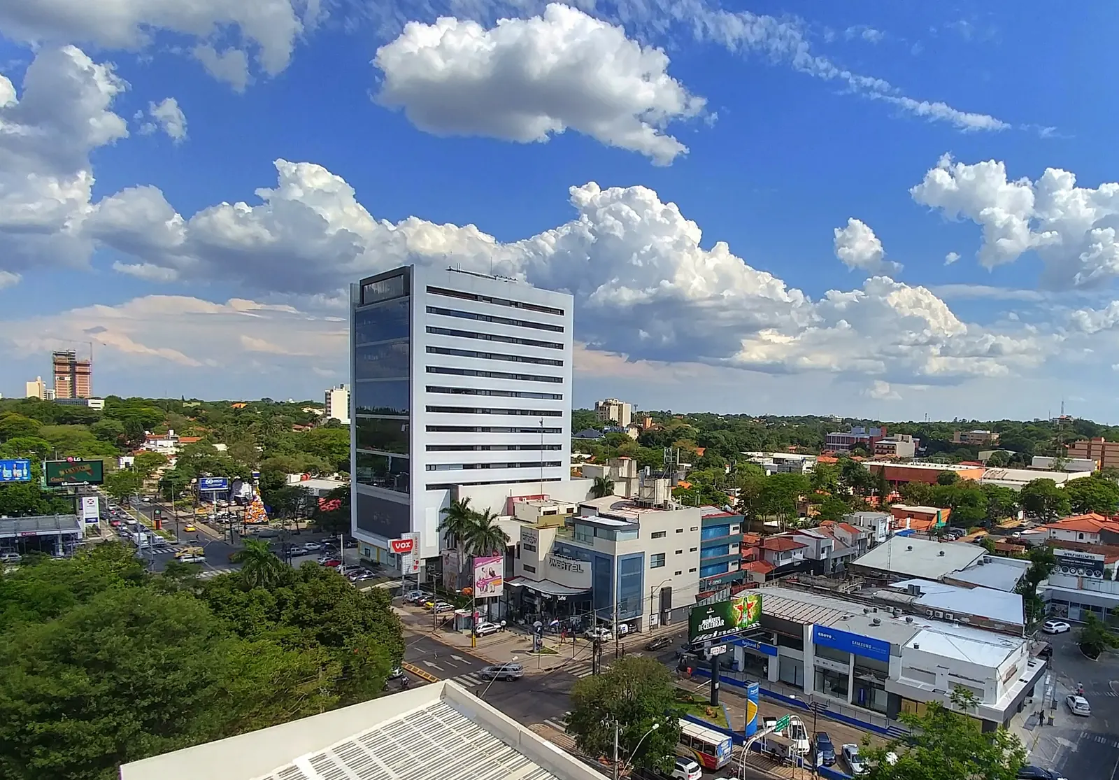 Elevated view over Villa Morra with a glass office tower, an avenue junction, low buildings and trees.